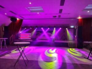 Een foto van het podium van de Foute Party 2023 in een lege zaal. Met roze en groene lichtstralen.